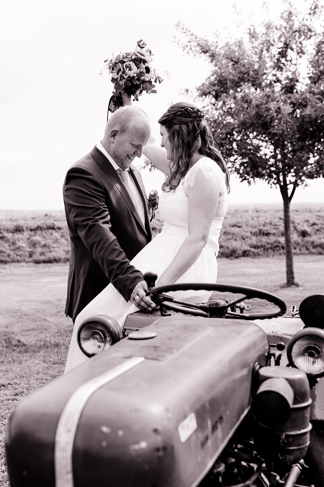 Braut sitzt auf Trecker, Bräutigam steht vor ihr