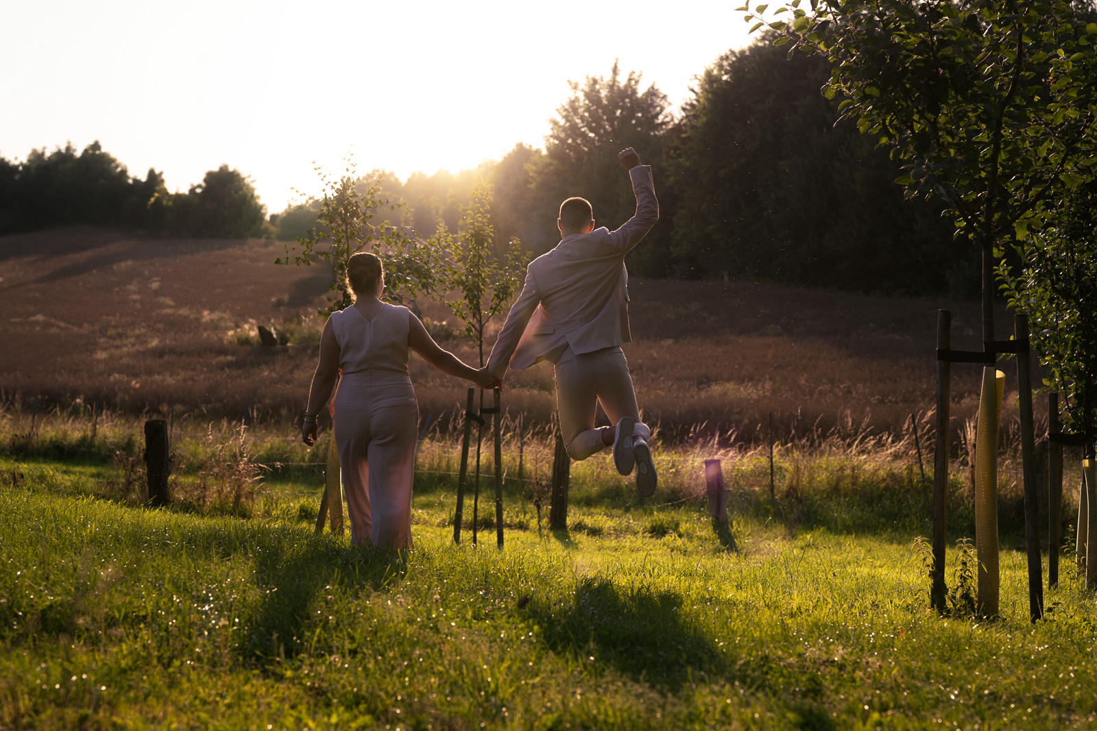 Paar läuft Hand in Hand eine Wiese entlang, Mann springt dabei hoch